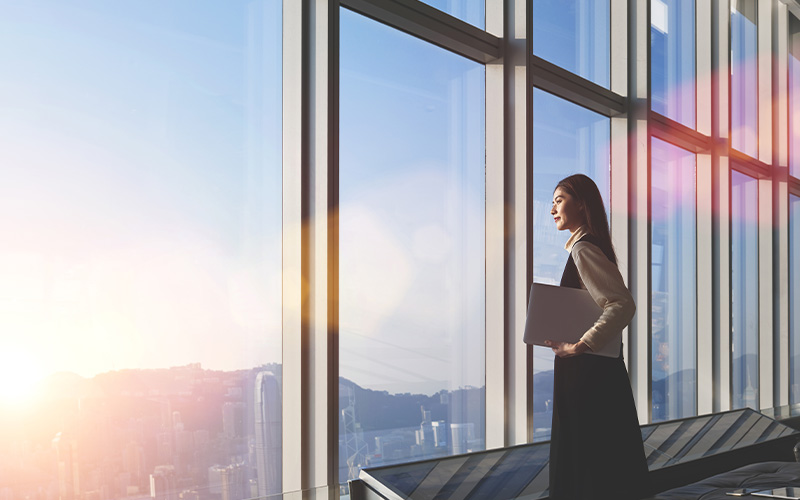 Woman holding a laptop while looking out of a window