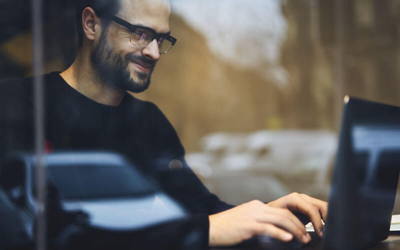 Smiling man in glasses works on laptop computer